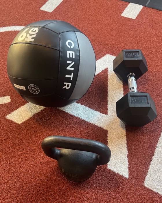 Wall ball de 6&nbsp;kg homologuée Hyrox, haltère de 15&nbsp;kg et kettlebell posés sur la piste du cabinet.